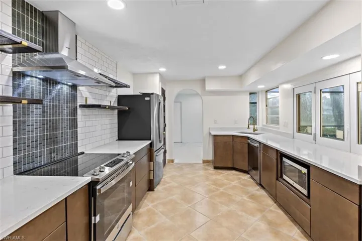 Kitchen featuring light tile patterned floors, wall chimney range hood, backsplash, appliances with stainless steel finishes, and sink