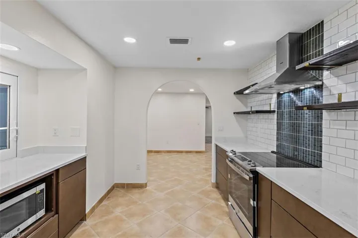 Kitchen with light tile patterned flooring, wall chimney exhaust hood, decorative backsplash, and stainless steel appliances