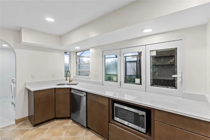 Kitchen with light tile patterned flooring, dark brown cabinets, washer / clothes dryer, stainless steel appliances, and sink