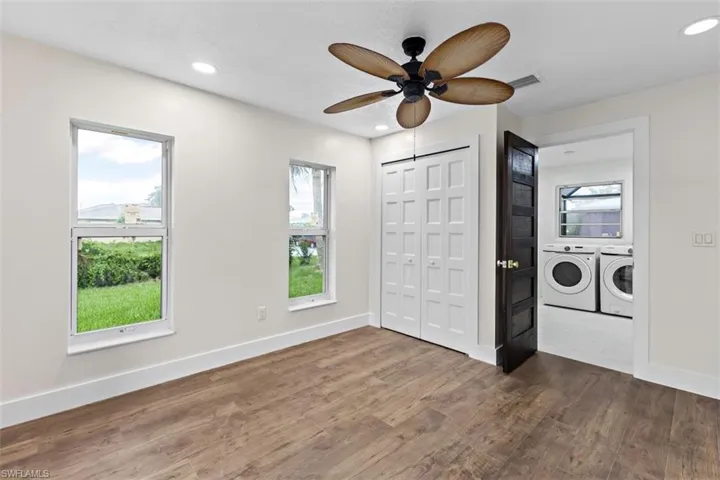 Unfurnished bedroom featuring ceiling fan, multiple windows, hardwood / wood-style flooring, and washer and dryer