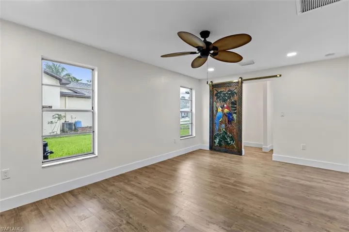 Unfurnished room with ceiling fan, a wealth of natural light, light wood-type flooring, and a barn door