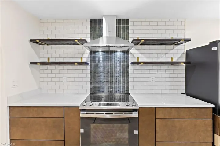 Kitchen featuring stainless steel electric range oven, black refrigerator, decorative backsplash, and wall chimney exhaust hood