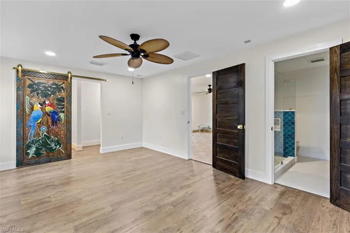 Unfurnished bedroom with light hardwood / wood-style floors, connected bathroom, a barn door, and ceiling fan
