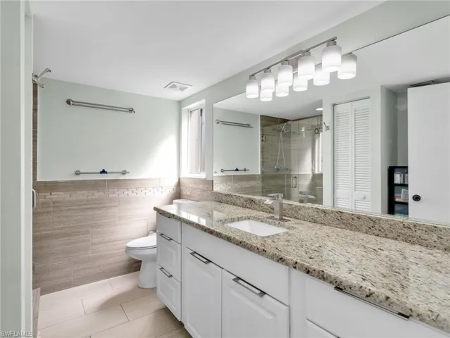 Bathroom with a closet, vanity, a shower stall, tile walls, and wainscoting