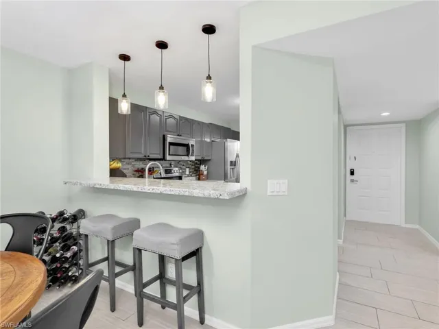 Kitchen featuring backsplash, stainless steel appliances, hanging light fixtures, gray cabinets, and a kitchen breakfast bar