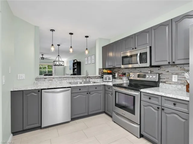 Kitchen with gray cabinets, stainless steel appliances, pendant lighting, and tasteful backsplash