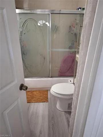 Bathroom with hardwood / wood-style flooring, toilet, and bath / shower combo with glass door
