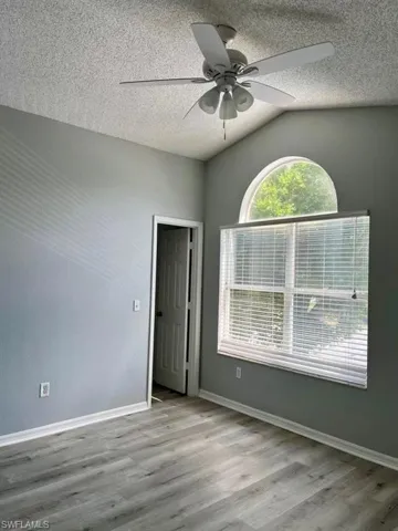 Empty room with a textured ceiling, wood finished floors, baseboards, and a ceiling fan