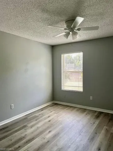 Spare room featuring a textured ceiling, baseboards, wood finished floors, and a ceiling fan