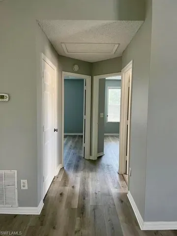 Hallway with a textured ceiling, visible vents, baseboards, wood finished floors, and attic access