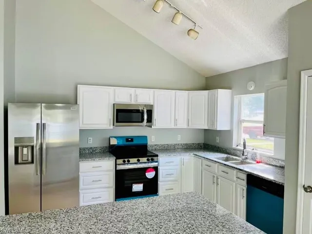 Kitchen featuring vaulted ceiling, light stone counters, a sink, appliances with stainless steel finishes, and white cabinets