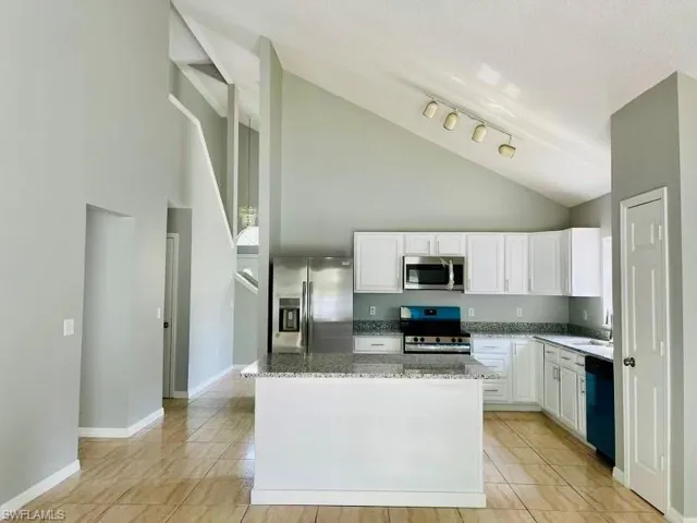 Kitchen featuring baseboards, white cabinetry, light stone countertops, and stainless steel appliances
