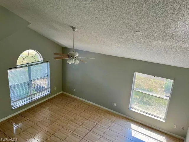 Spare room with baseboards, lofted ceiling, a textured ceiling, and a ceiling fan