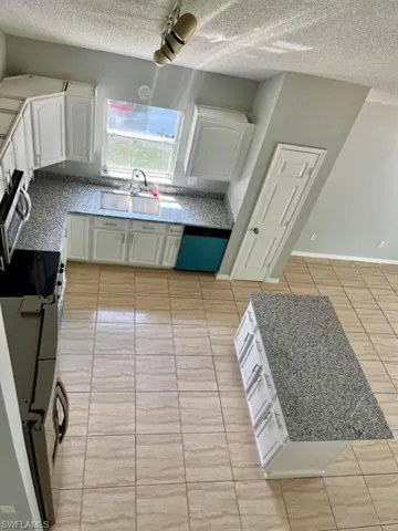Kitchen featuring a sink, white cabinetry, dishwasher, a textured ceiling, and light tile patterned floors