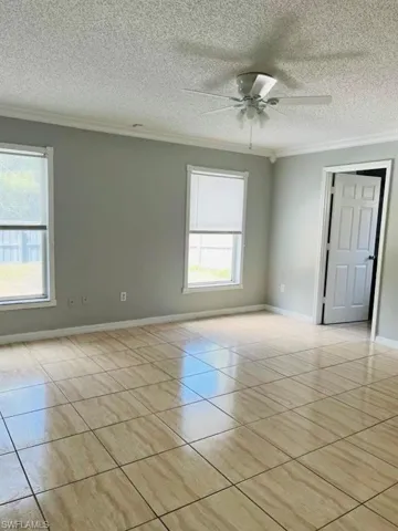 Empty room featuring a ceiling fan, light tile patterned flooring, ornamental molding, and baseboards