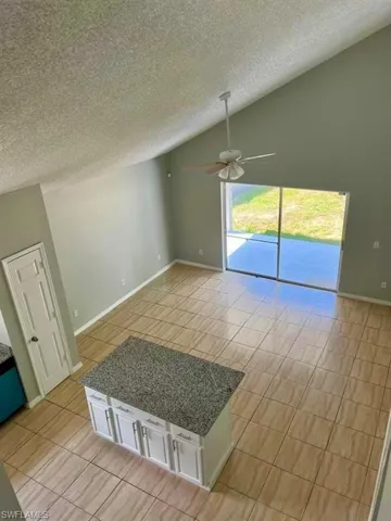 Kitchen with light tile patterned flooring, a ceiling fan, white cabinetry, a textured ceiling, and lofted ceiling