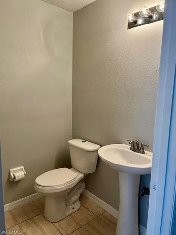 Half bath featuring baseboards, toilet, a textured wall, and tile patterned floors