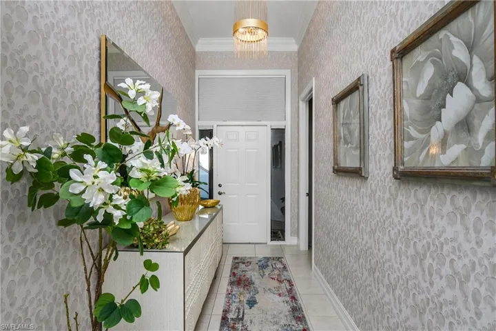 Entrance foyer featuring a notable chandelier, light tile patterned flooring, ornamental molding, and wallpapered walls