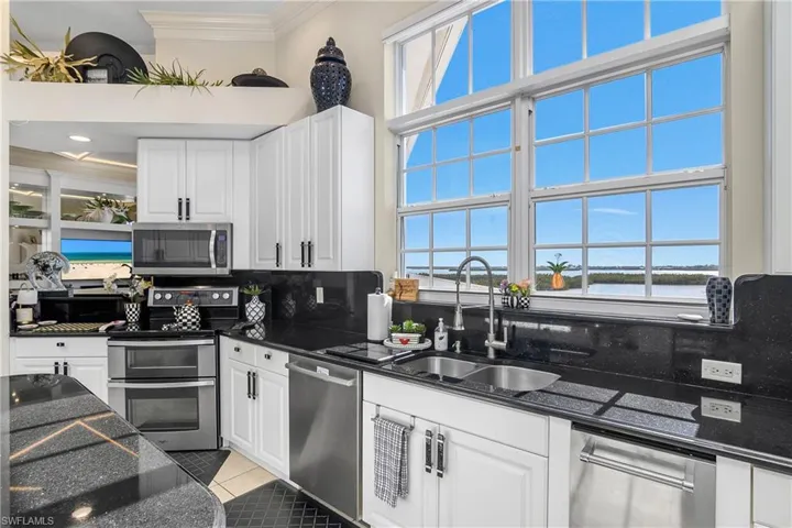 Kitchen featuring a water view, a sink, stainless steel appliances, crown molding, and light tile patterned floors