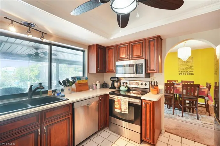 Kitchen with stainless steel appliances, ceiling fan, arched walkways, light countertops, and light tile patterned floors