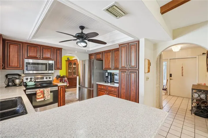 Kitchen with appliances with stainless steel finishes, arched walkways, light countertops, and a tray ceiling