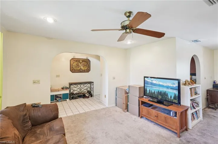 Living room featuring arched walkways, a ceiling fan, carpet, and tile patterned floors