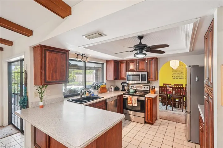 Kitchen with appliances with stainless steel finishes, a peninsula, light countertops, healthy amount of natural light, and beamed ceiling