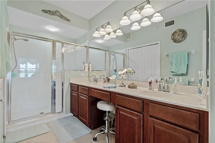 Bathroom with double vanity, a shower stall, light tile patterned floors, and a closet