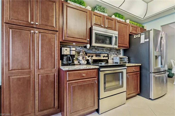 Kitchen featuring stainless steel appliances, light stone counters, light tile patterned floors, tasteful backsplash, and wood finish cabinetry