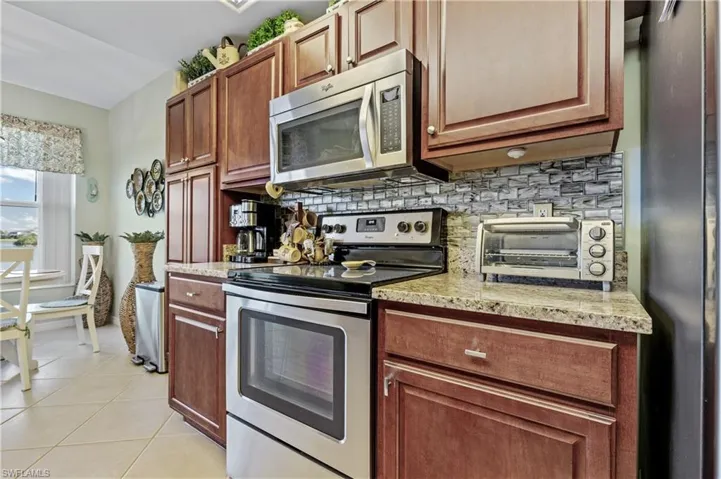 Kitchen with stainless steel appliances, light stone counters, light tile patterned floors, and tasteful backsplash