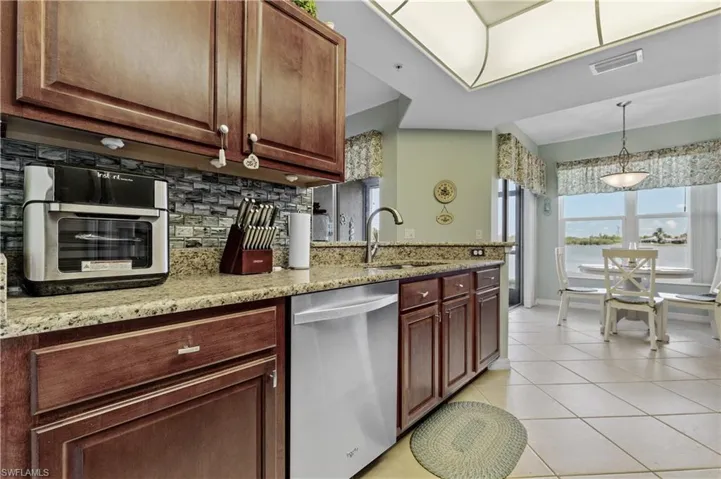 Kitchen with stainless steel dishwasher, light stone counters, light tile patterned floors, and pendant lighting
