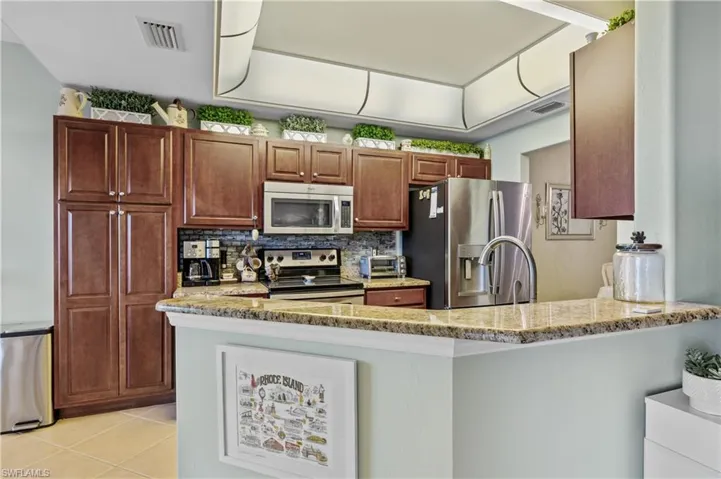 Kitchen featuring stainless steel appliances, light stone countertops, a peninsula, and tasteful backsplash