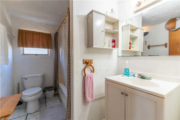 Full bathroom with vanity, toilet, shower / bath combo with shower curtain, and a textured ceiling