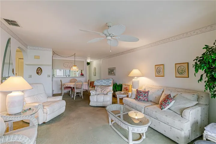 Carpeted living room featuring ceiling fan and arched walkways
