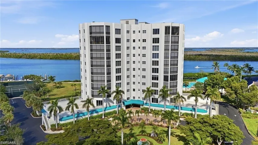 Waterfront high-rise building featuring a contemporary design, multiple balconies, a swimming pool, and surrounding tropical landscaping