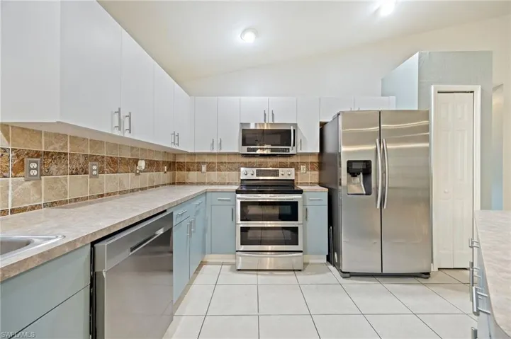 Kitchen featuring appliances with stainless steel finishes, backsplash, light countertops, light tile patterned flooring, and vaulted ceiling