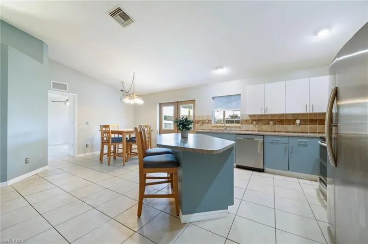Kitchen with appliances with stainless steel finishes, lofted ceiling, tasteful backsplash, light tile patterned floors, and a center island