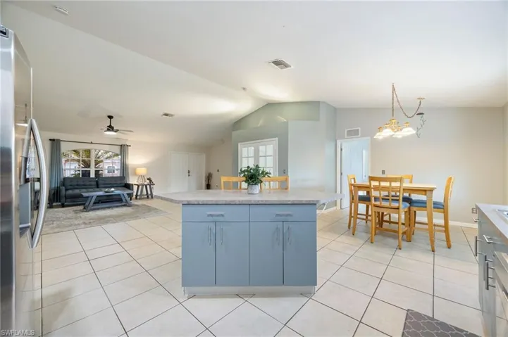 Kitchen featuring vaulted ceiling, freestanding refrigerator, light tile patterned flooring, open floor plan, and a center island