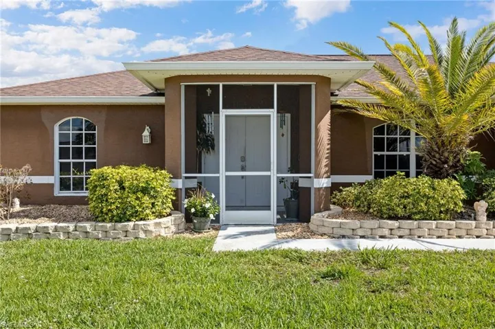 View of exterior entry with stucco siding, a yard, and roof with shingles