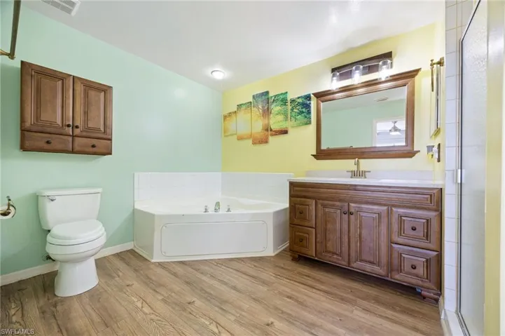 Full bathroom with wood finished floors, a bath, toilet, and baseboards