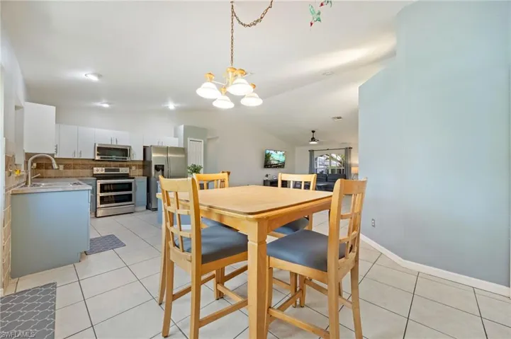 Dining area featuring a chandelier, light tile patterned flooring, vaulted ceiling, and a ceiling fan
