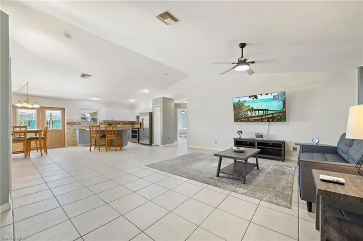 Living room with lofted ceiling, light tile patterned floors, ceiling fan, baseboards, and a chandelier