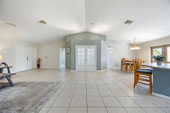 Living room featuring lofted ceiling, french doors, light tile patterned floors, a chandelier, and a ceiling fan