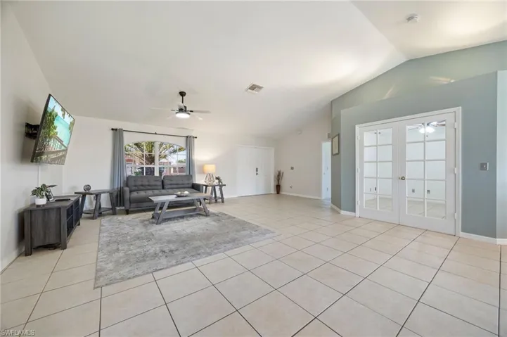 Living area featuring a ceiling fan, lofted ceiling, light tile patterned floors, french doors, and baseboards