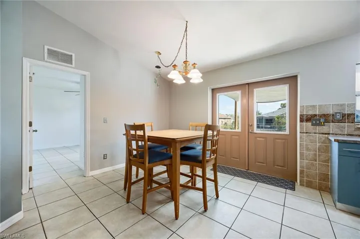 Dining area featuring light tile patterned flooring, a chandelier, tile walls, and french doors