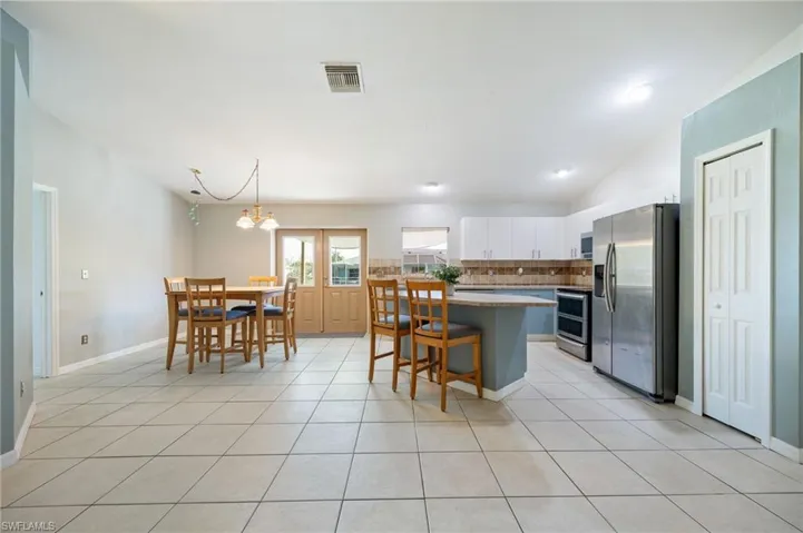 Kitchen featuring stainless steel appliances, tasteful backsplash, white cabinetry, vaulted ceiling, and light tile patterned floors