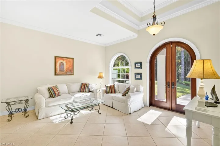 Living room featuring french doors, crown molding, tile patterned floors, and arched walkways