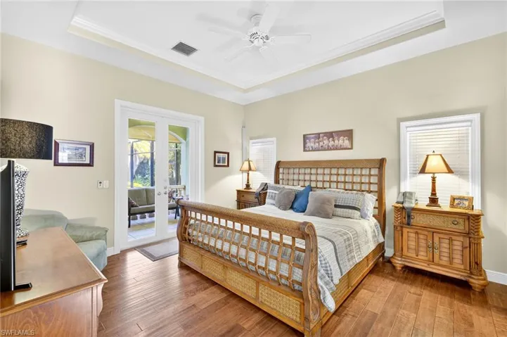 Bedroom with a tray ceiling, crown molding, french doors, wood finished floors, and ceiling fan