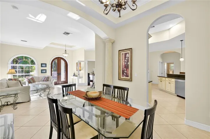 Dining room featuring ornamental molding, a chandelier, light tile patterned floors, arched walkways, and a raised ceiling