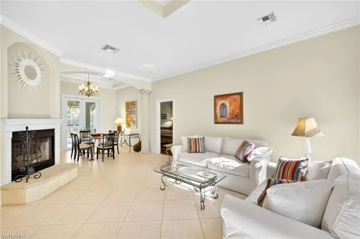 Living area featuring ornamental molding, a fireplace with raised hearth, light tile patterned floors, arched walkways, and a chandelier
